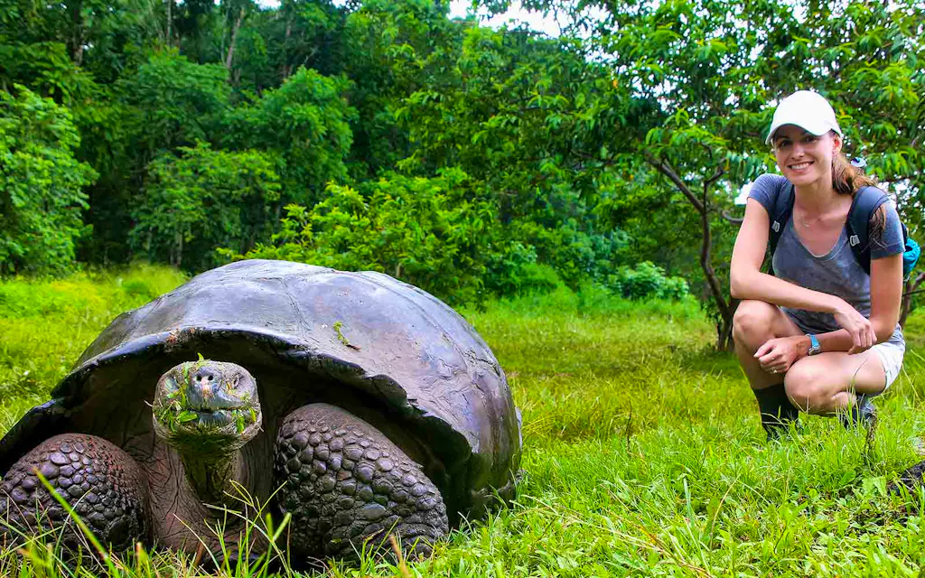 A woman kneeling down next to a giant tortoise.