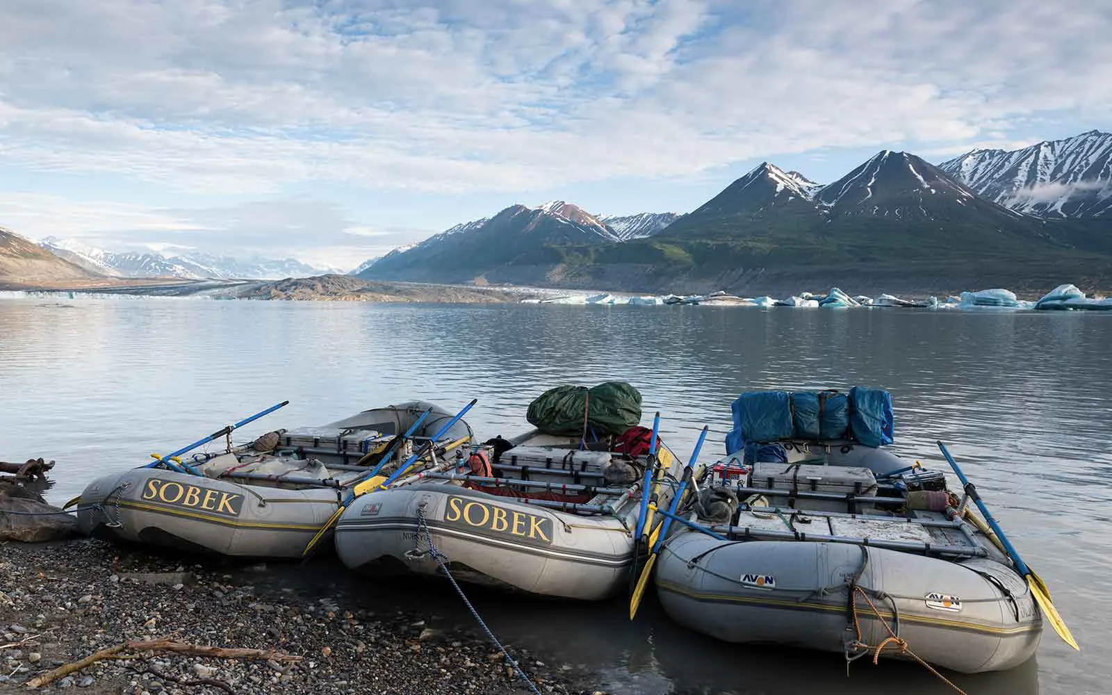 Three rafts on the shore of a body of water with mountains in the background.