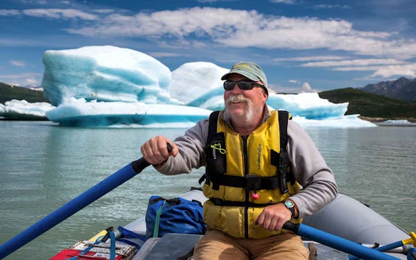 A man on a raft in front of an iceberg.