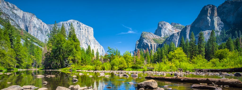 Classic view of scenic Yosemite Valley with famous El Capitan rock climbing summit and idyllic Merced river on a sunny day with blue sky and clouds in summer Yosemite National Park California USA.