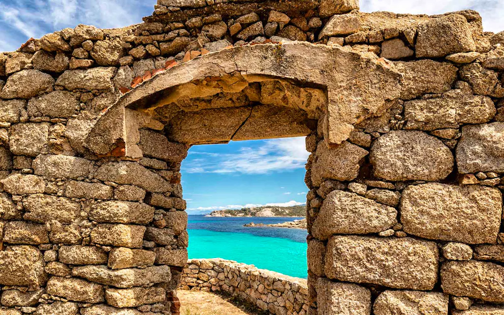 A stone arch structure on the hiking trail in Corsica, France with the Mediterranean Sea in the background. 