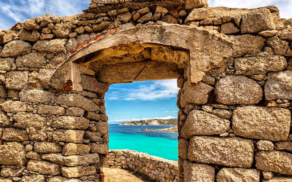 A stone arch structure on the hiking trail in Corsica, France with the Mediterranean Sea in the background. 