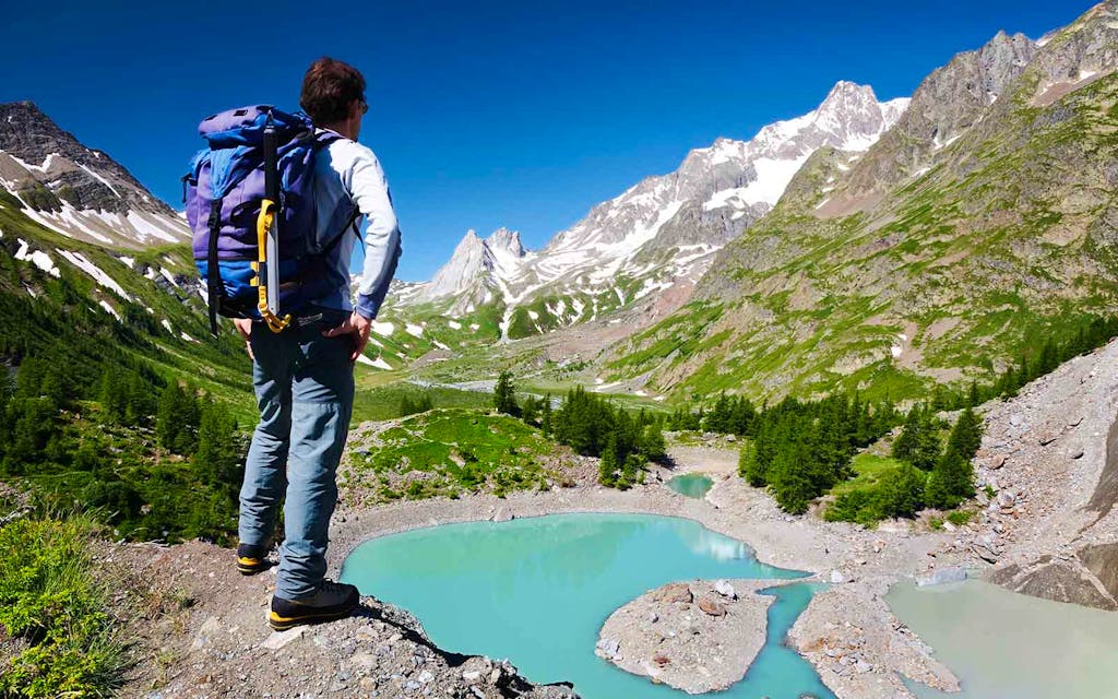 Man hiking in France on the Tour du Mont Blanc trail looking at a glacier mountain lake. 