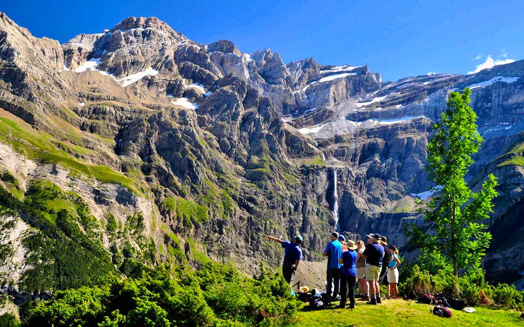 A group of people standing in front of a majestic mountain with a breathtaking waterfall, exploring one of the best hikes in France.