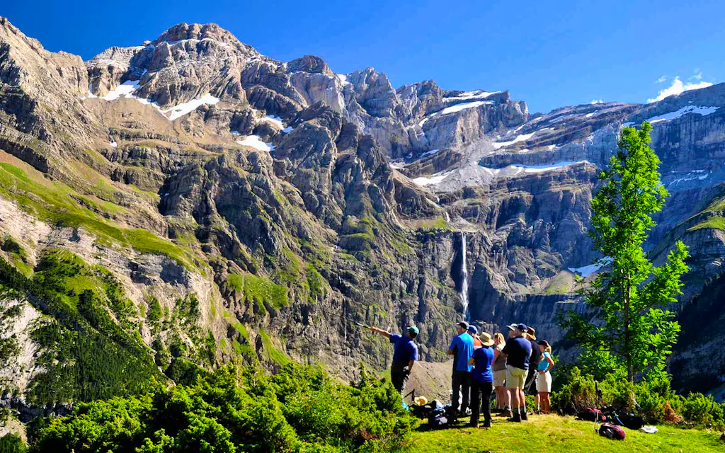 A group of people standing in front of a majestic mountain with a breathtaking waterfall, exploring one of the best hikes in France.