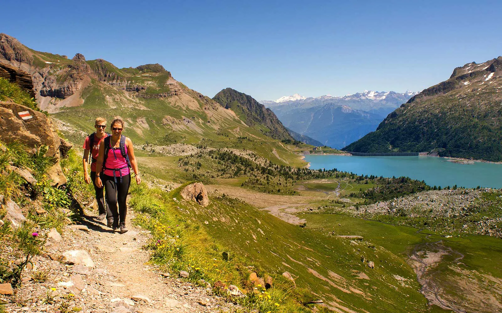 Two hikers on a trekking tour walking along a trail with a lake in the background.