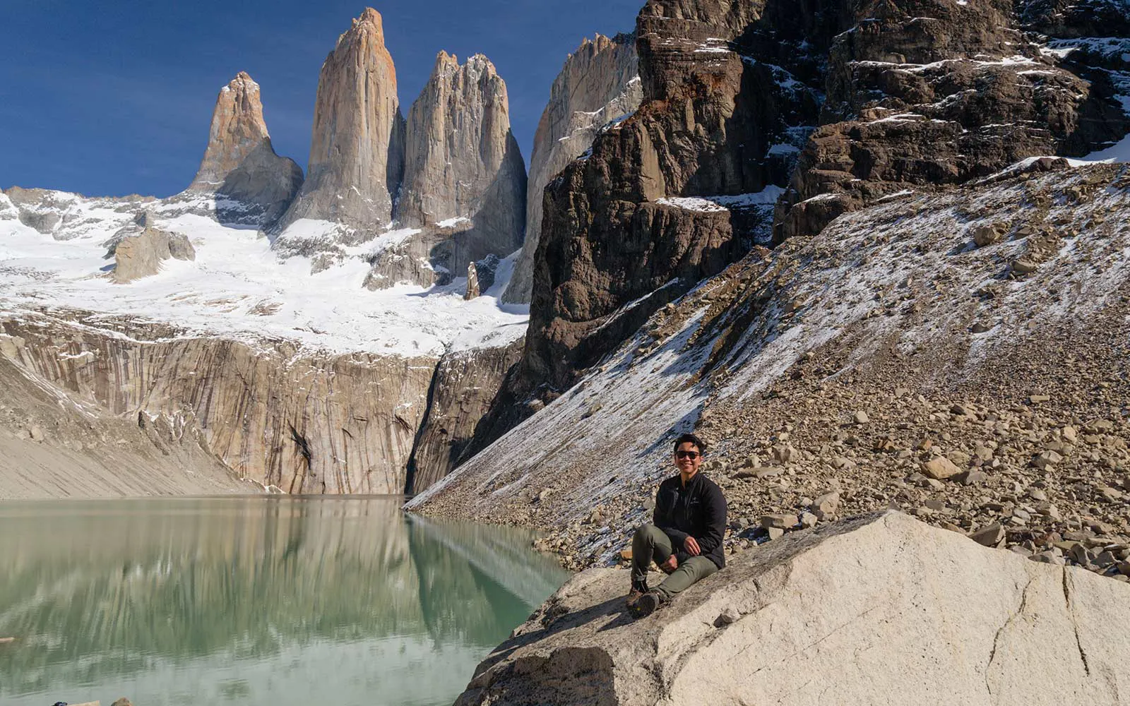 A man sitting on a rock overlooking a serene lake during a hiking tour.