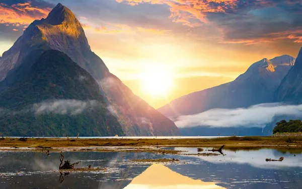 The sun rises over the mountains in milford sound, new zealand.