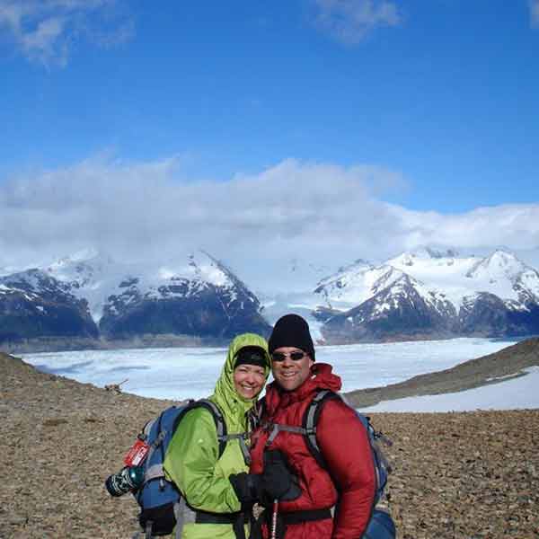 Two people standing in front of a mountain with mountains in the background.