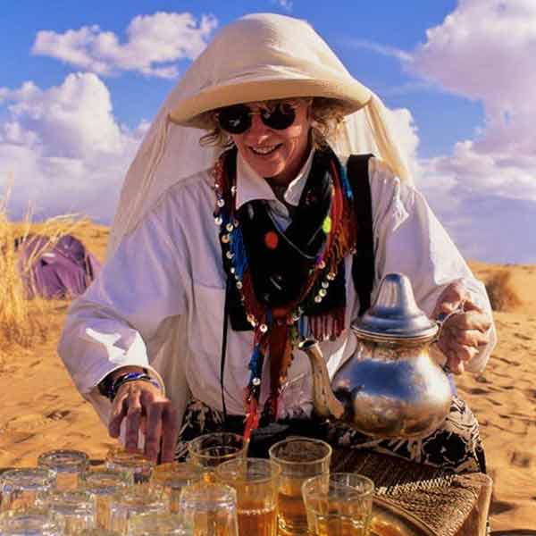 A woman in a hat is serving tea in the desert.