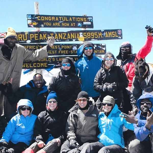 A group of people posing for a photo on the summit of mt kilimanjaro.