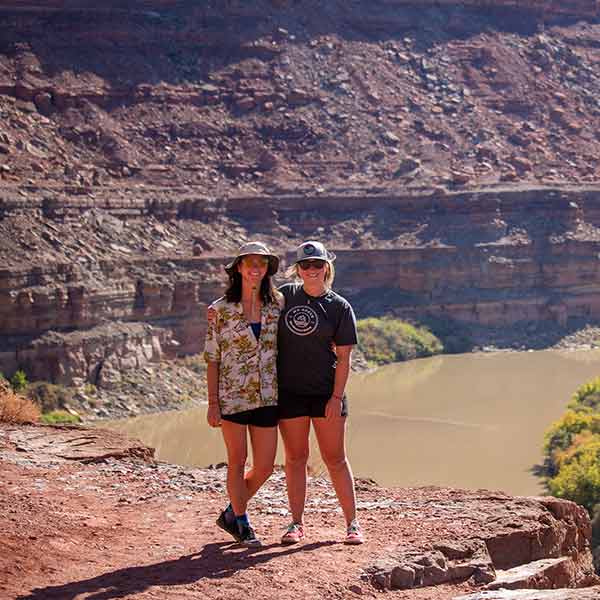 Two women standing in front of a canyon with a river.