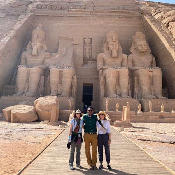 Three people standing in front of a large sphinx in egypt.