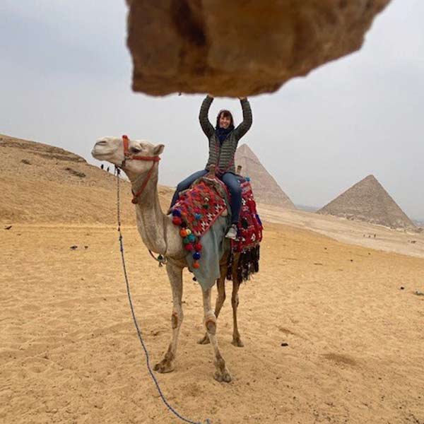 A woman riding a camel in front of the pyramids.