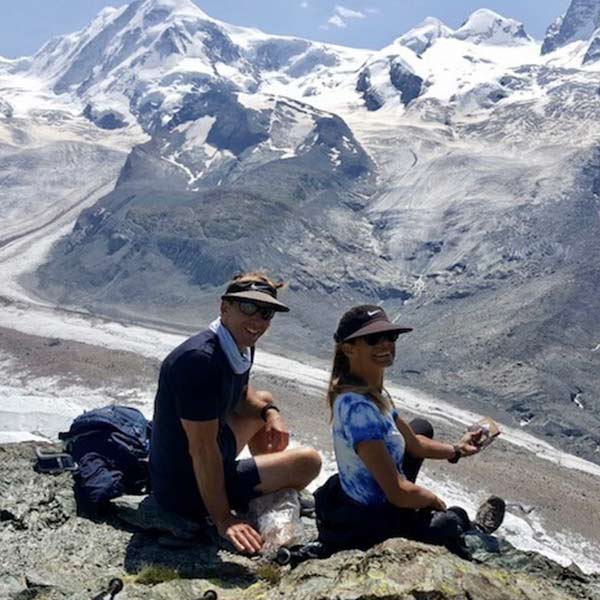 Two people sitting on top of a rock with mountains in the background.