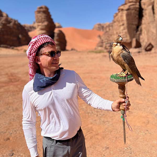 A man holding a falcon in the desert.