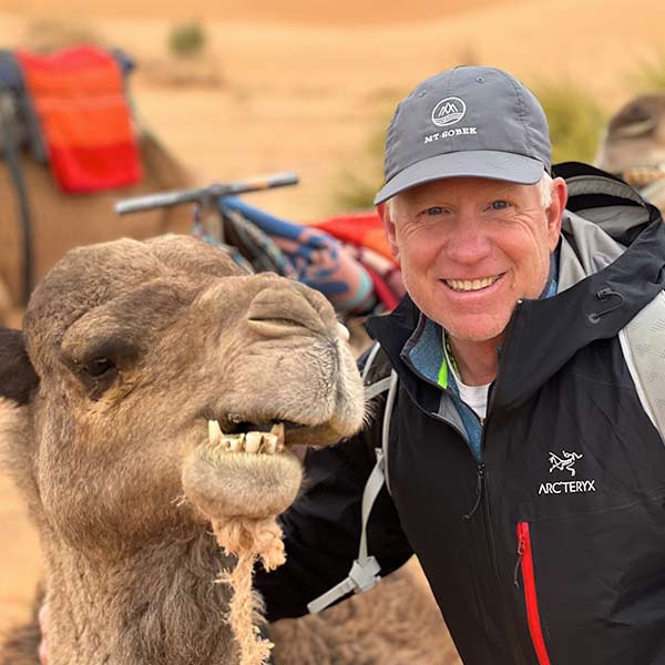 A man smiling next to a camel in the desert.