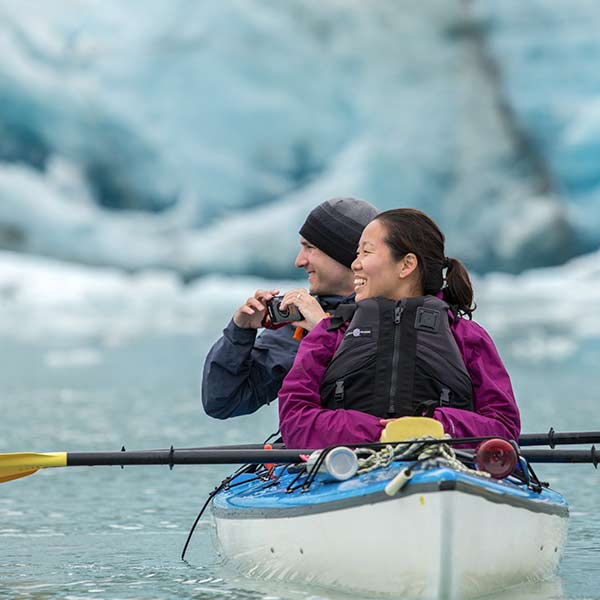 A couple in a kayak in front of an iceberg.