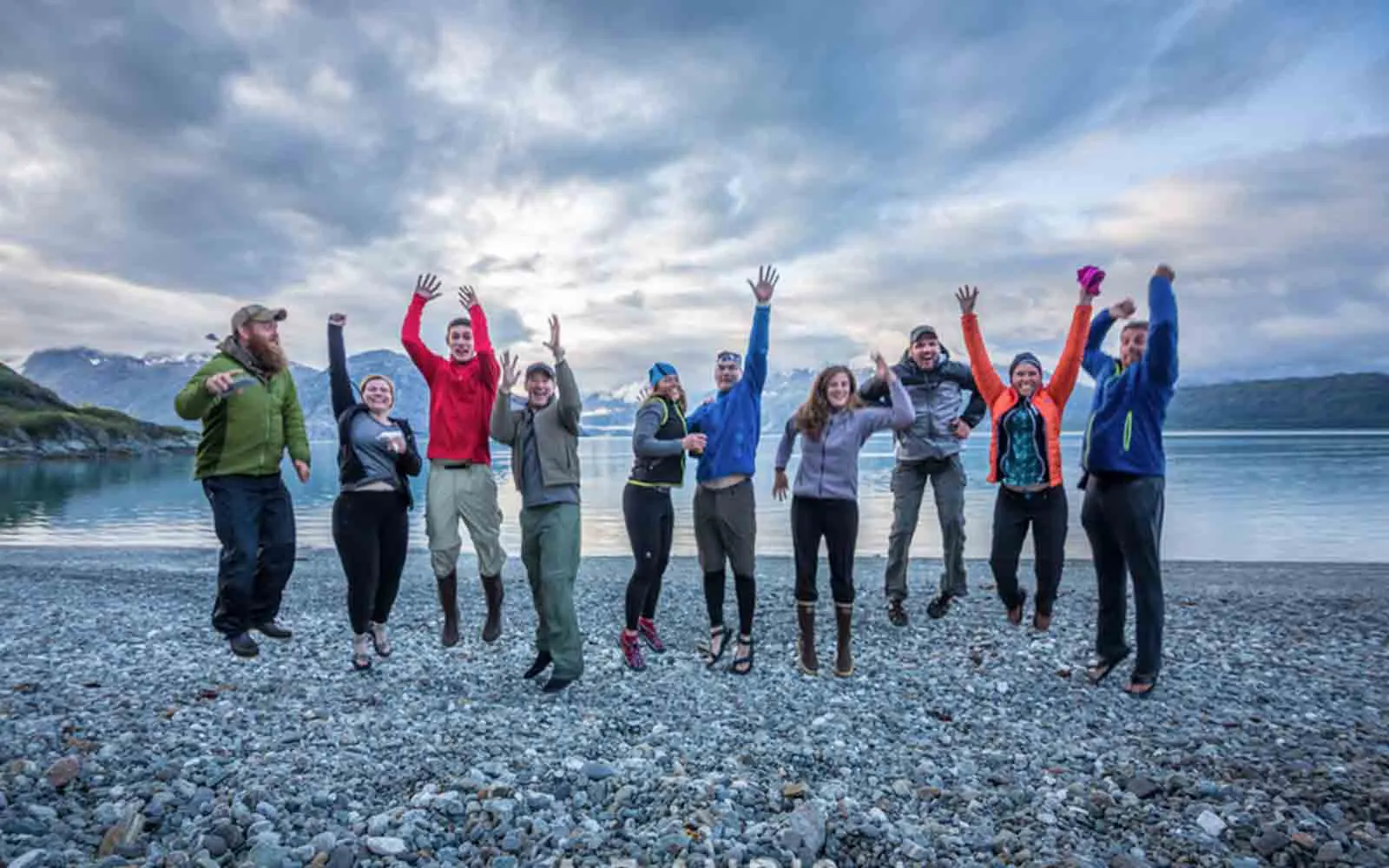 A group of people jumping in the air near a lake.