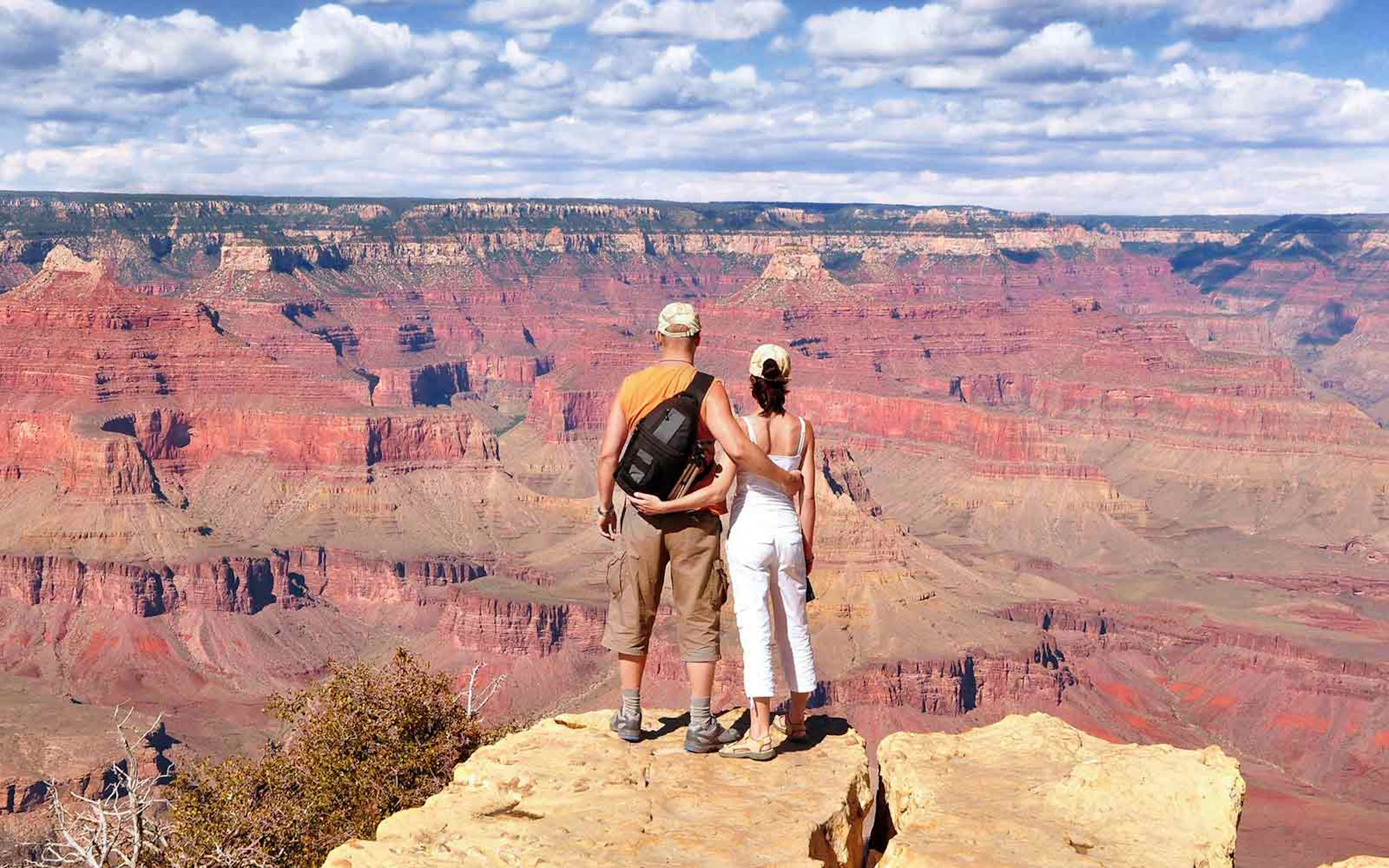 Two people standing on a cliff overlooking the grand canyon.