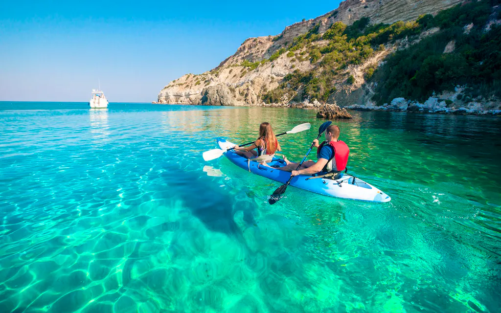 Two people are kayaking in the clear blue water.