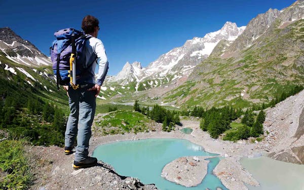 A man is standing on a cliff overlooking a lake, experiencing one of the best alps hiking adventures.