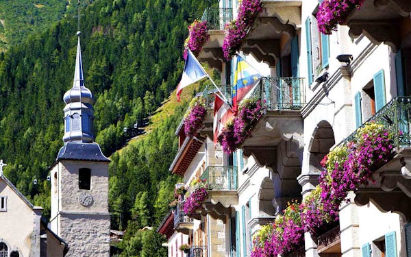A picturesque building with a clock tower in the heart of the best alps hiking adventures, boasting beautifully adorned balconies adorned with vibrant flowers.