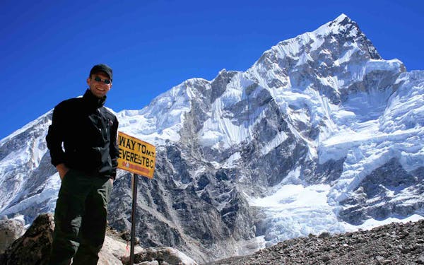 A man standing in front of a mountain with a sign.