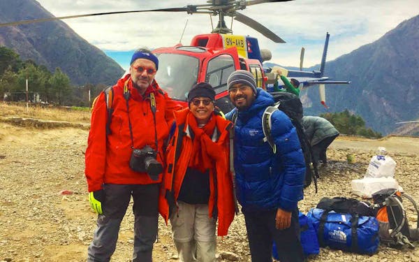 Three people standing in front of a Nepal Trekking helicopter.