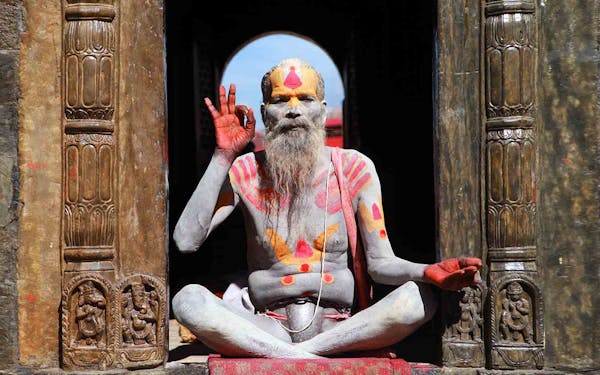 A man with a painted face sits in front of a door during his Nepal Trekking Adventure.