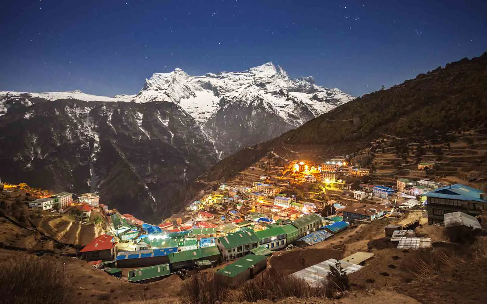 A Nepal village lit up at night with mountains in the background, offering breathtaking Nepal trekking adventures.