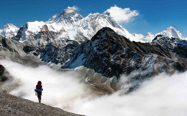 A person enjoying Nepal Trekking Adventures on top of a mountain with clouds in the background.
