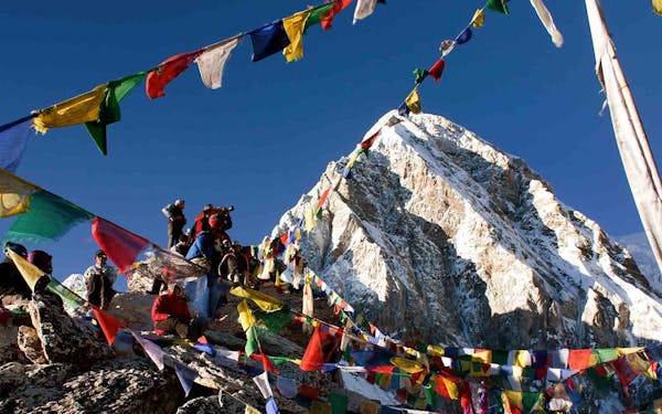 A group of people on a Nepal trekking adventure, standing on top of a mountain adorned with prayer flags.