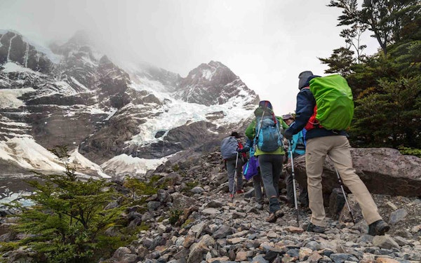 A group of people hiking up a rocky path near a snowy mountain, experiencing active adventures in Patagonia.