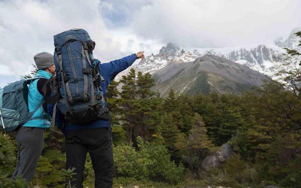 Two adventurous hikers with backpacks pointing at a majestic mountain in Patagonia, one of the best active adventures in the region.