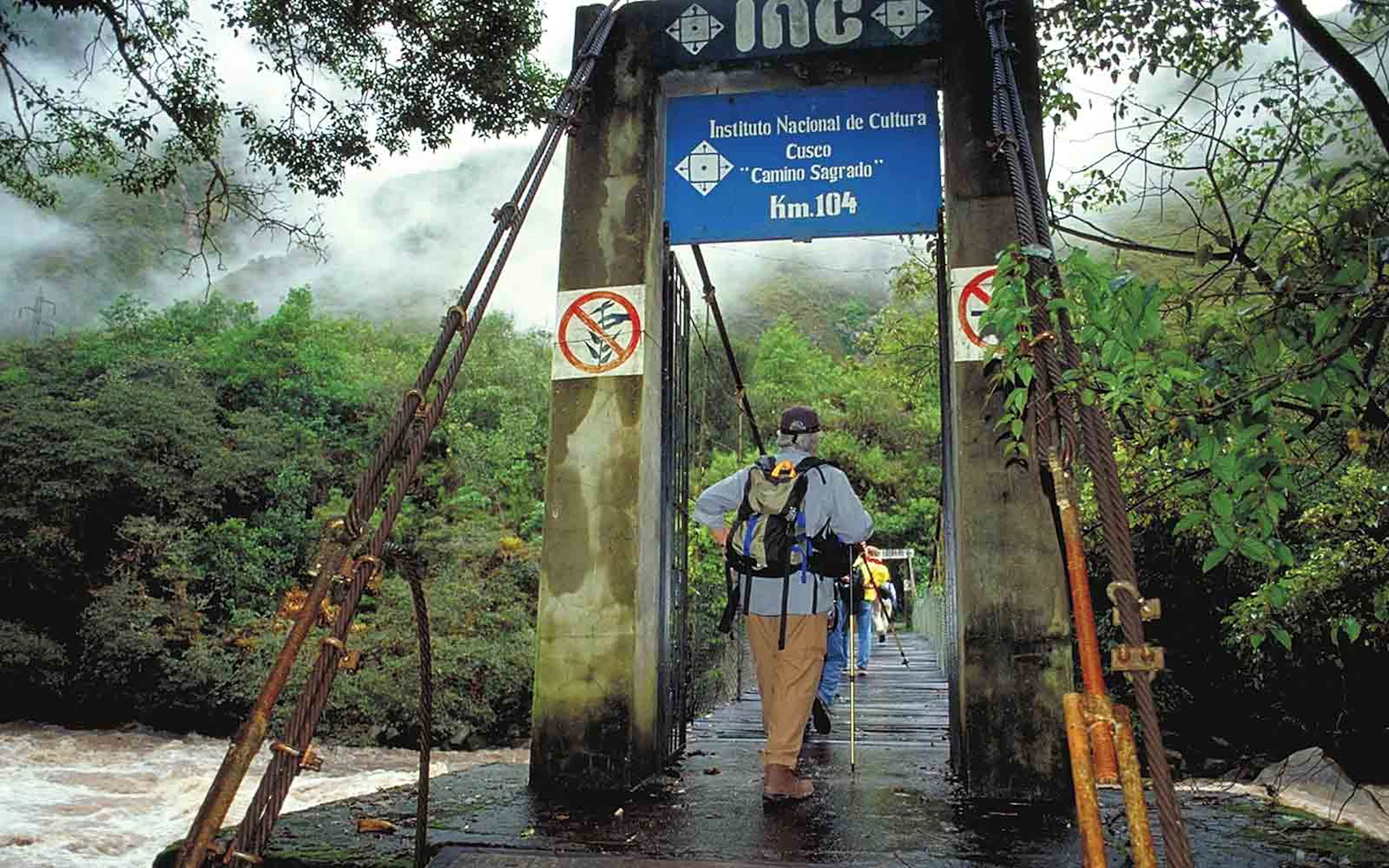 A man walking on a bridge over a river.