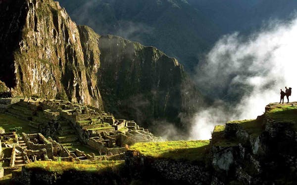 Two people standing on a cliff overlooking machu picchu.