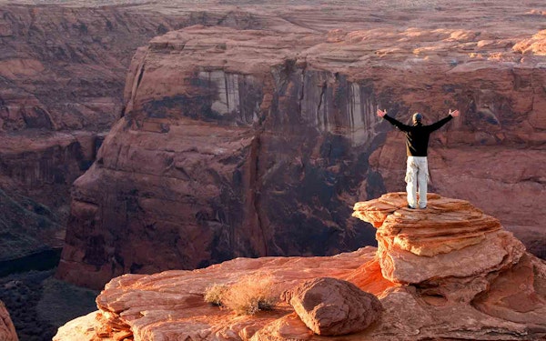 A man standing on top of a cliff in a national park, with his arms outstretched, embracing the grandeur of nature during his adventurous journey.