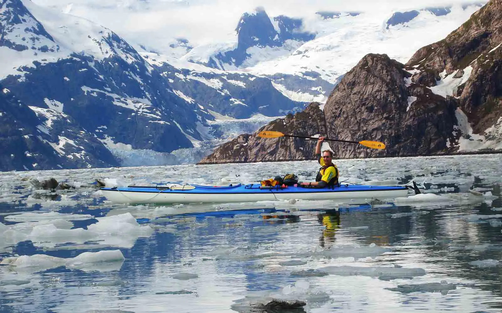 A man in a kayak in the middle of a body of water with icebergs in the background, embarking on a thrilling national park adventure.