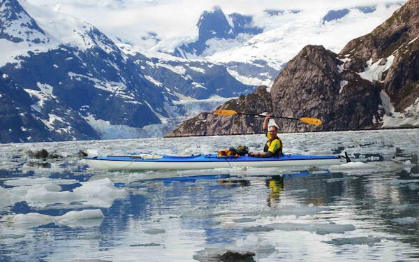 A man in a kayak in the middle of a body of water with icebergs in the background, embarking on a thrilling national park adventure.