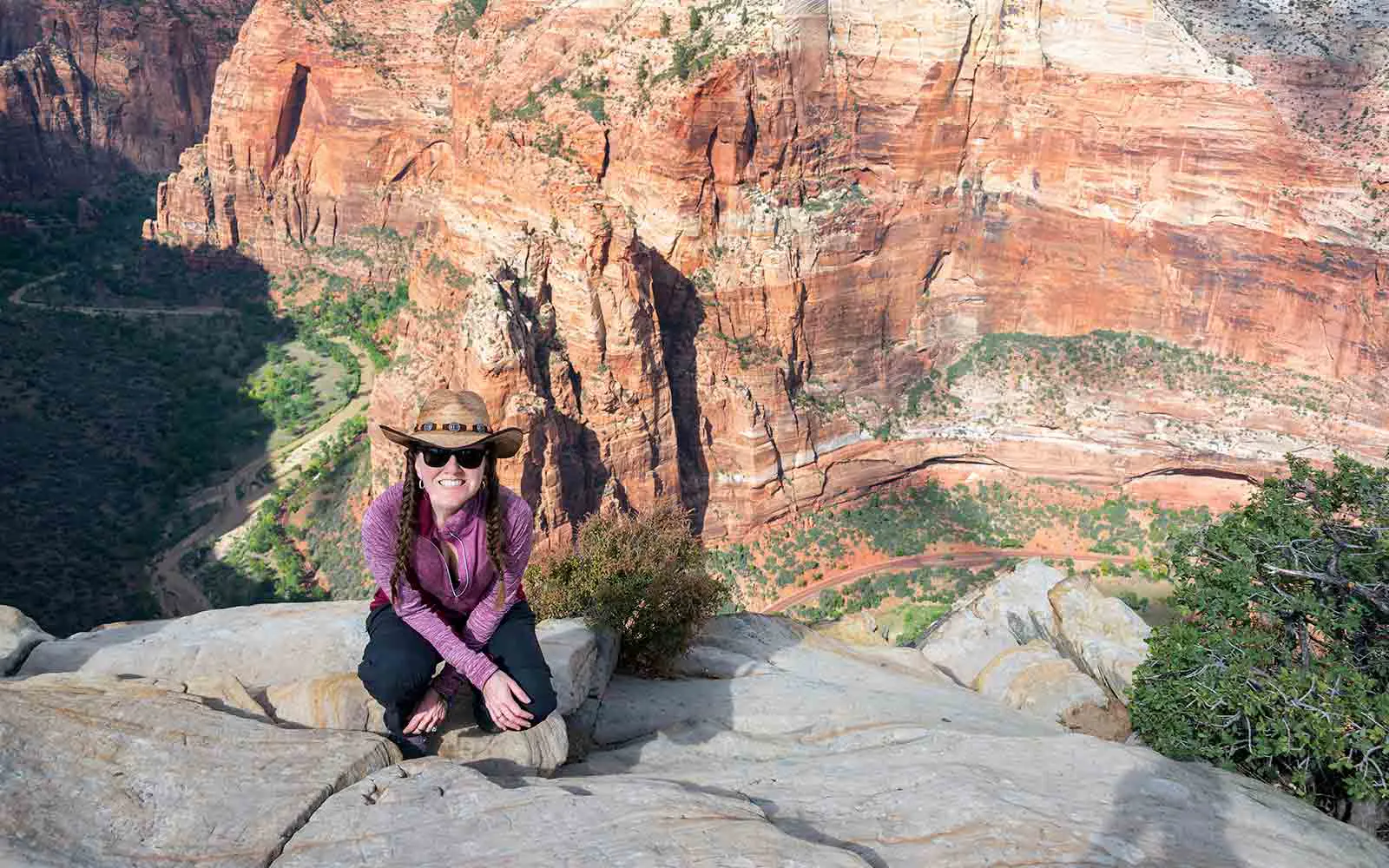 A woman in a hat sits on top of a cliff overlooking a National Park canyon.