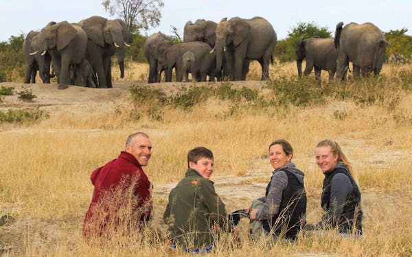 A group of people on an unforgettable Wildlife Safari Adventure, posing with majestic elephants in the background.