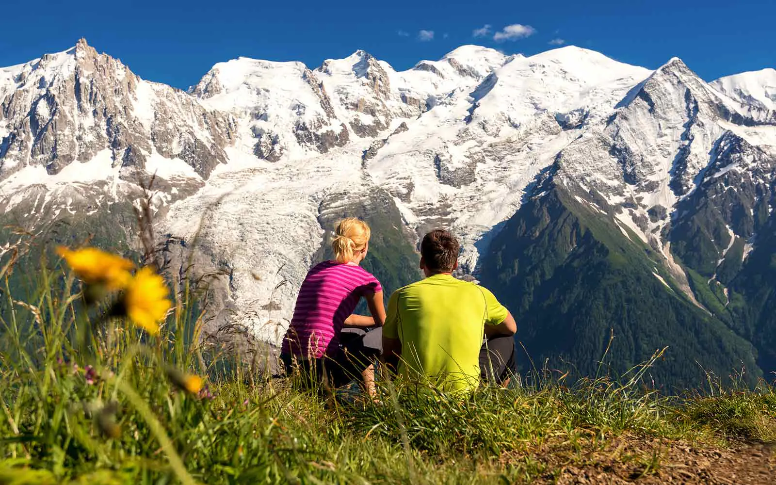 Two people enjoying the stunning view of the mountains while sitting on a grassy hill in one of the best hiking spots in Switzerland.