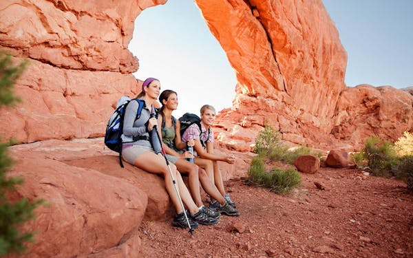 Three hikers sitting on a rock in Arches National Park, Utah during an adventurous USA tour.