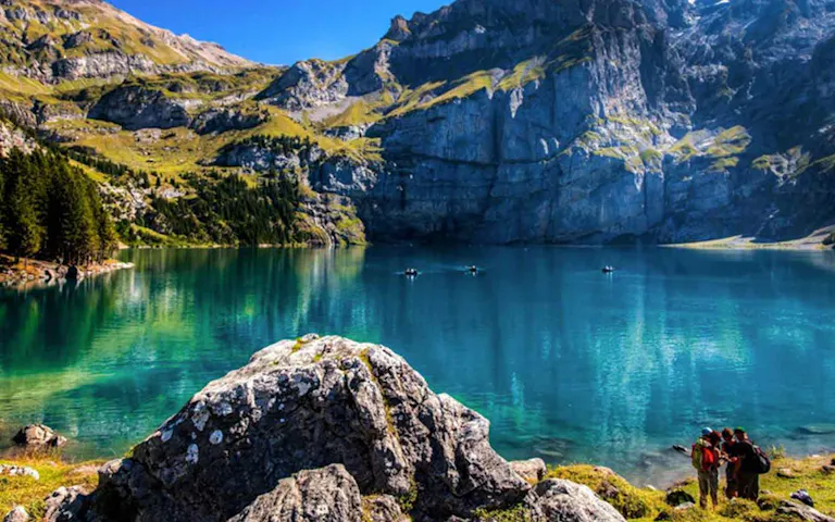 Hikers looking at a beautiful crystal clear blue glacial like high up on the Chindbetti Pass in the Alps