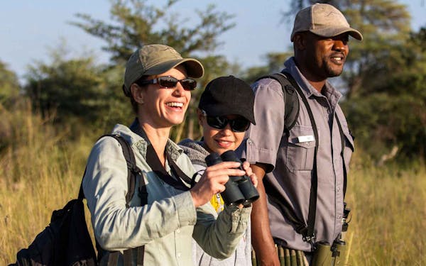 Three people with binoculars standing in an African field, embarking on an adventure travel.