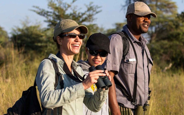 Three people with binoculars standing in an African field, embarking on an adventure travel.