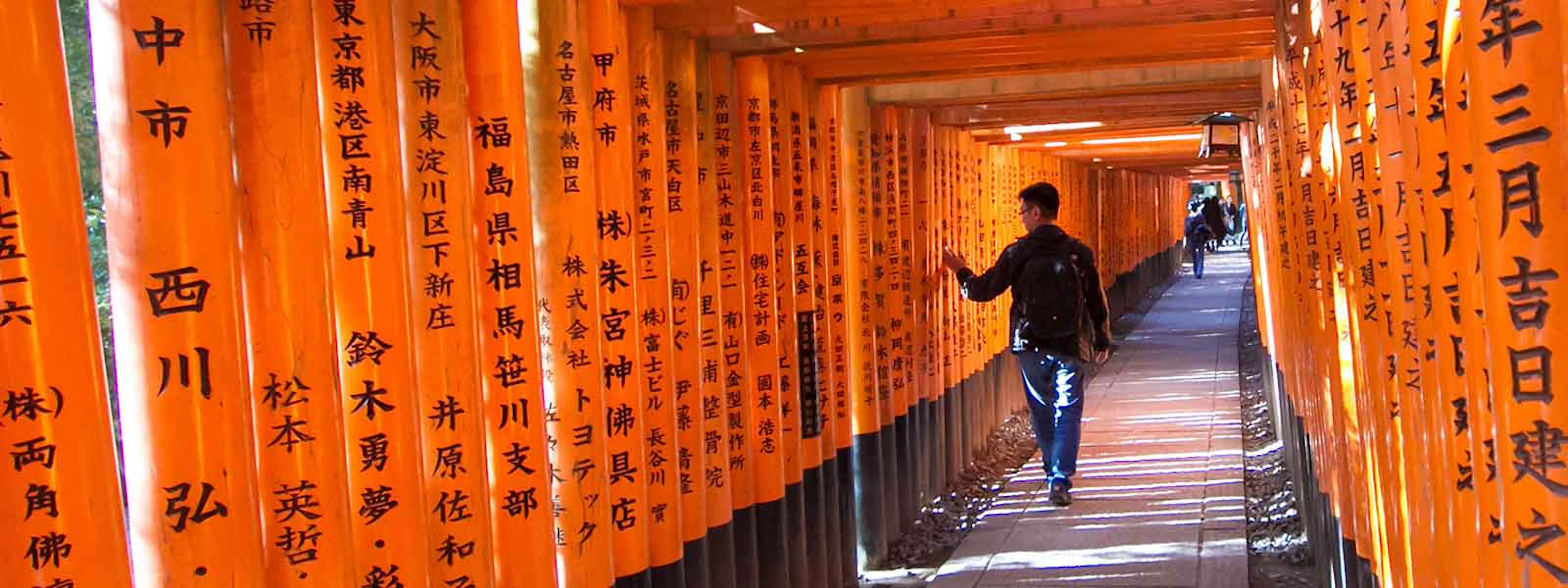 A man walking down a hallway with orange tori tori gates.
