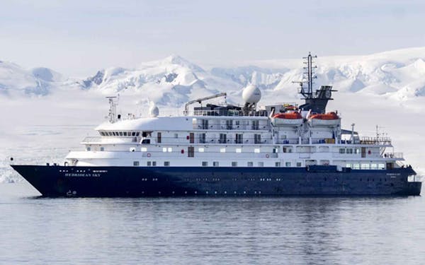 A polar cruise ship with snowy mountains in the background.