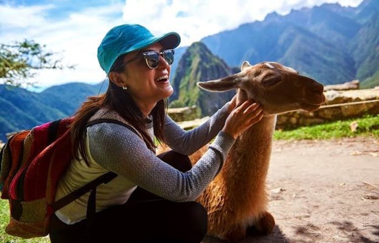 female hiker with a blue hat stroking a sacred llama near Machu Picchu